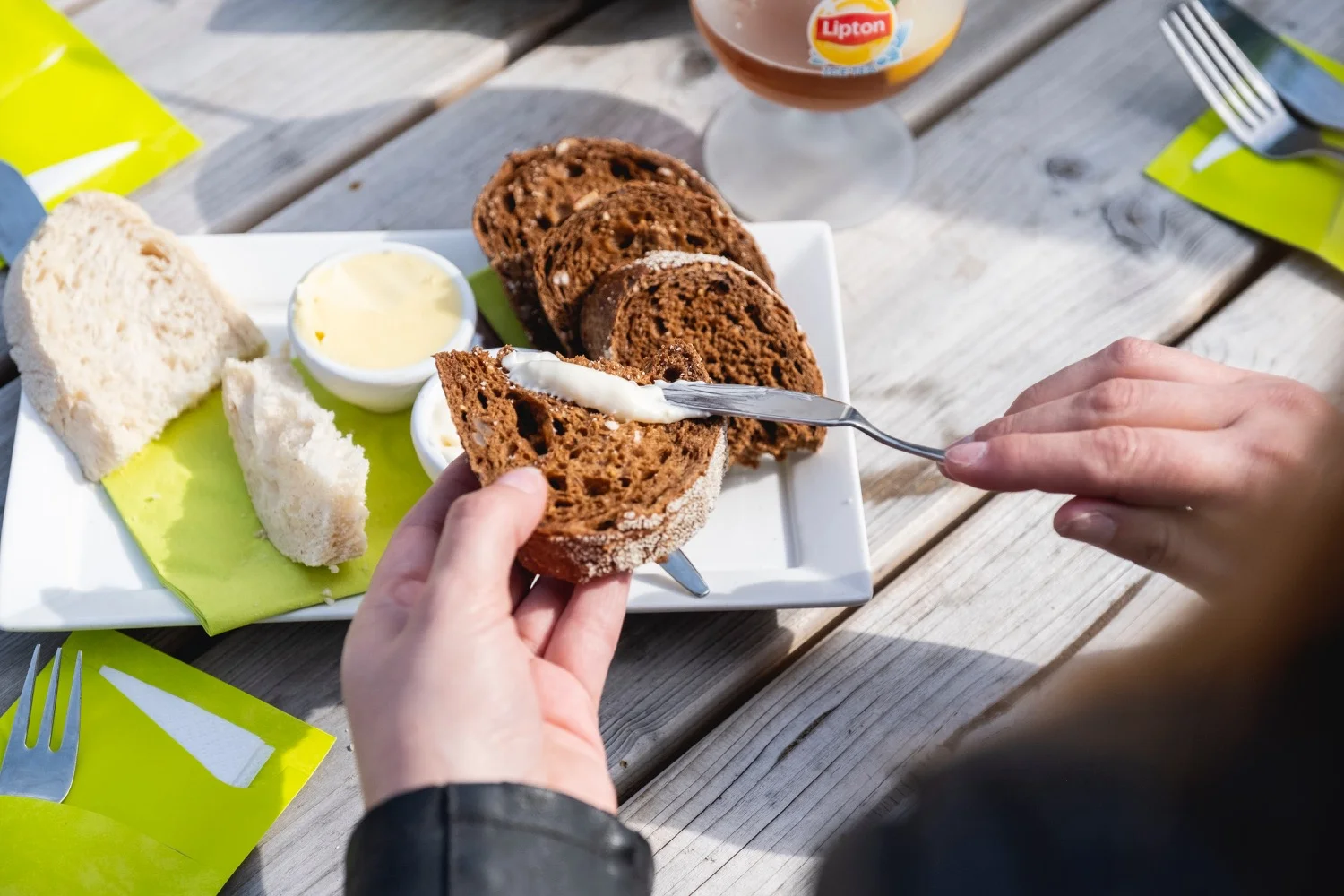 Handen besmeren een sneetje boerenbrood met gezouten boter